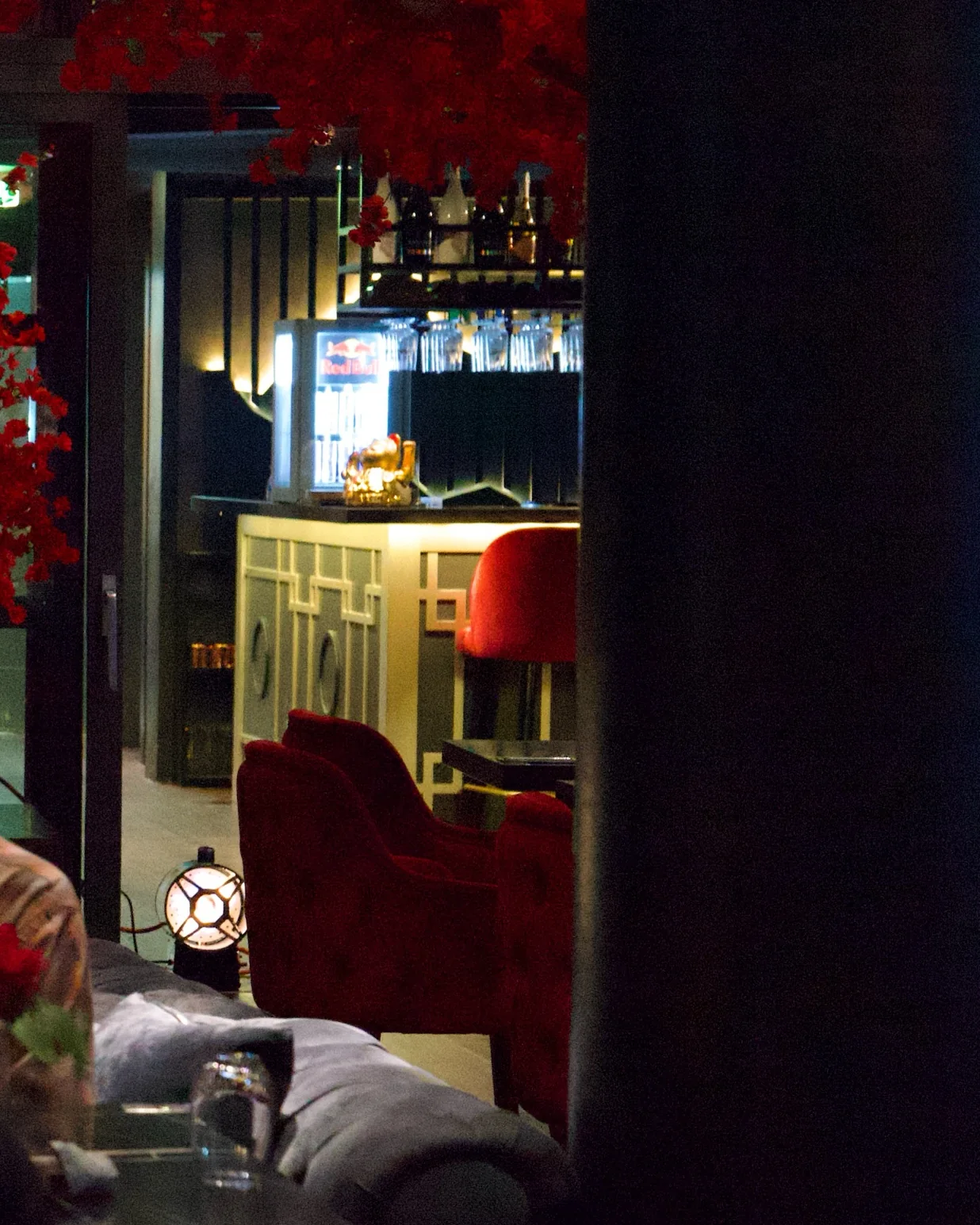 Die Bar am Abend: Flaschenregal, Messingtresen und roter Samtsessel