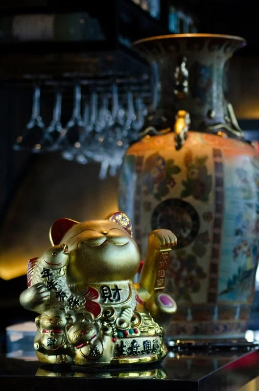 Goldene Winkekatze vor einer bemalten Vase im Regal hinter der Bar