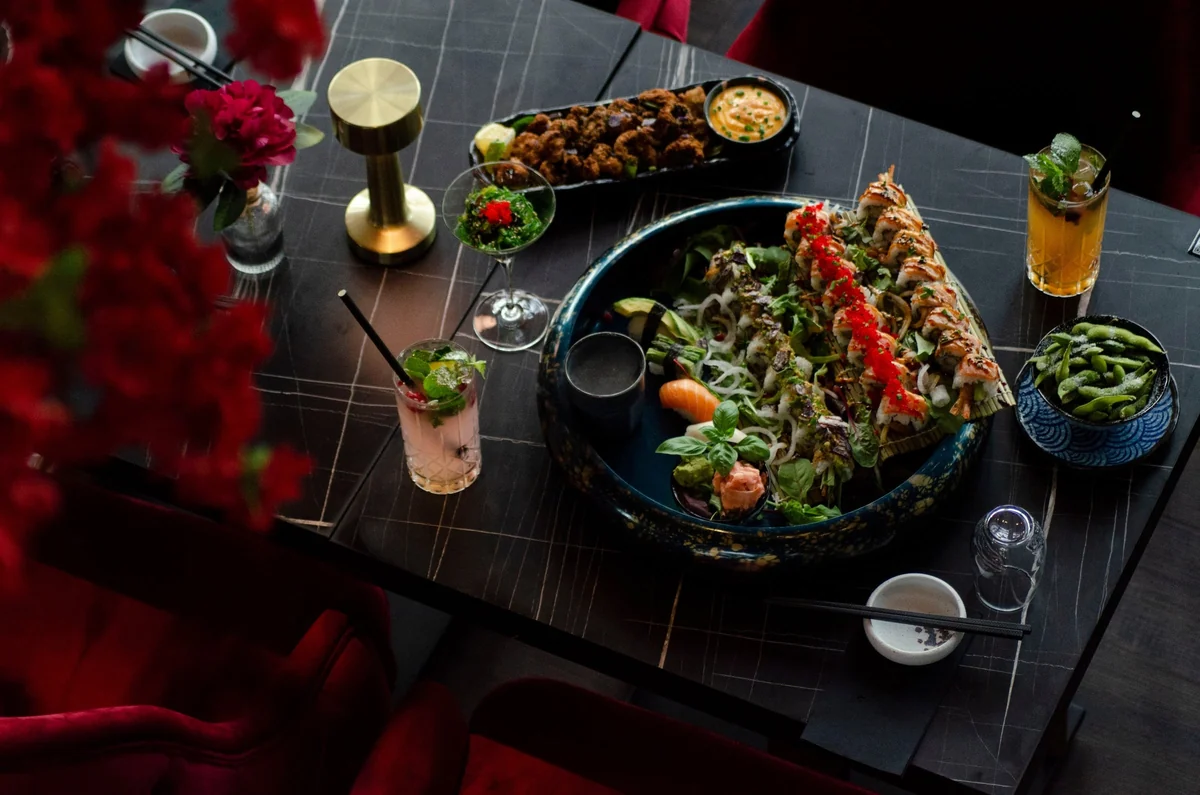 Gedeckter Marmortisch von oben mit Sushi-Platte, Karaage, Edamame und Cocktails